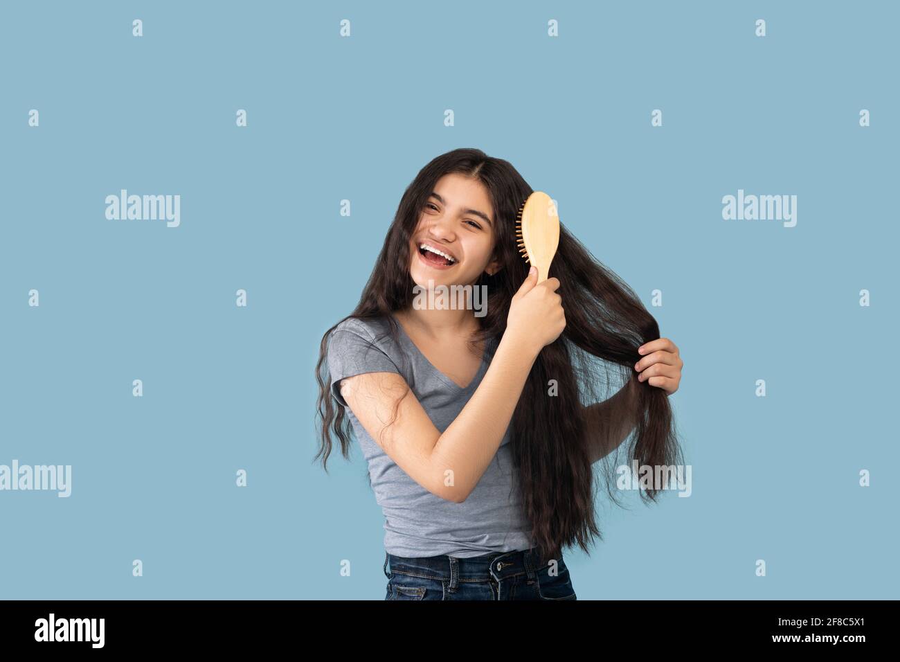 Attraktive indische Teenager-Mädchen Bürsten ihre langen Haare mit Holz Pinsel auf blauem Studiohintergrund Stockfoto