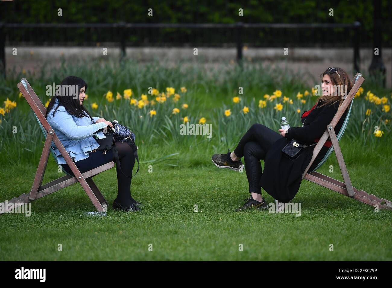 Zwei Frauen sitzen in Liegestühlen im Green Park, London. Bilddatum: Dienstag, 13. April 2021. Stockfoto