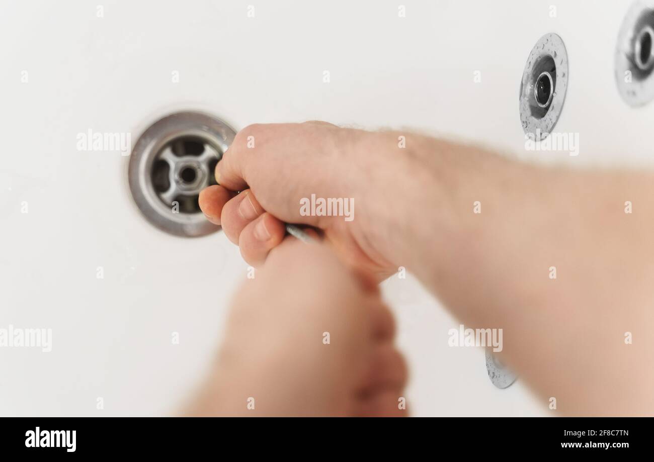 Klempner, der die Badewanne mit einer Abflussschlange entklumpt hat. Stockfoto