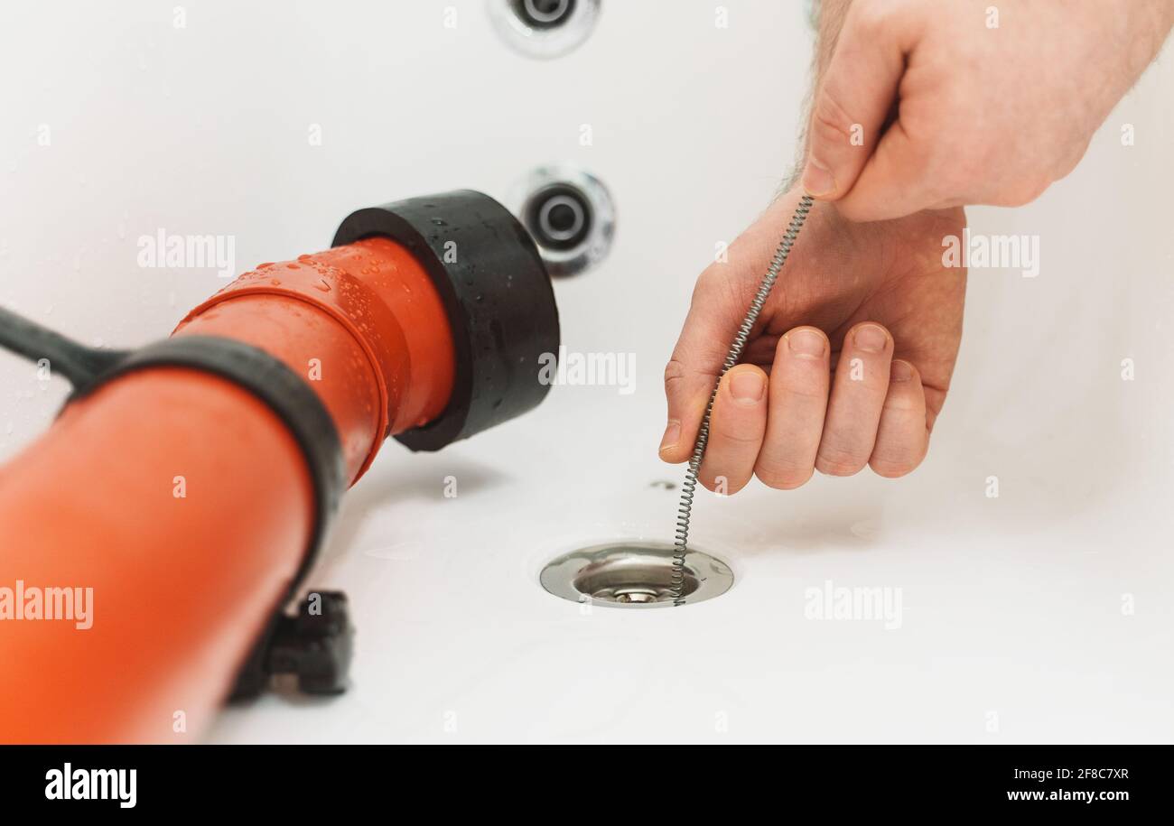 Klempner, der die Badewanne mit einer Abflussschlange entklumpt hat. Stockfoto