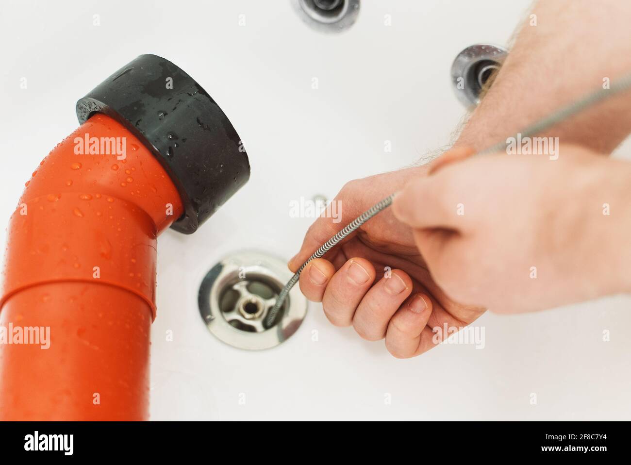 Klempner, der die Badewanne mit einer Abflussschlange entklumpt hat. Stockfoto