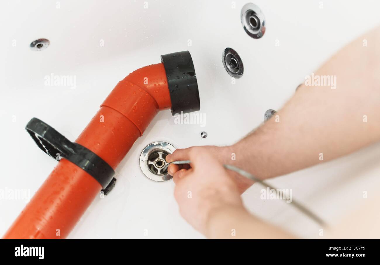 Klempner, der die Badewanne mit einer Abflussschlange entklumpt hat. Stockfoto