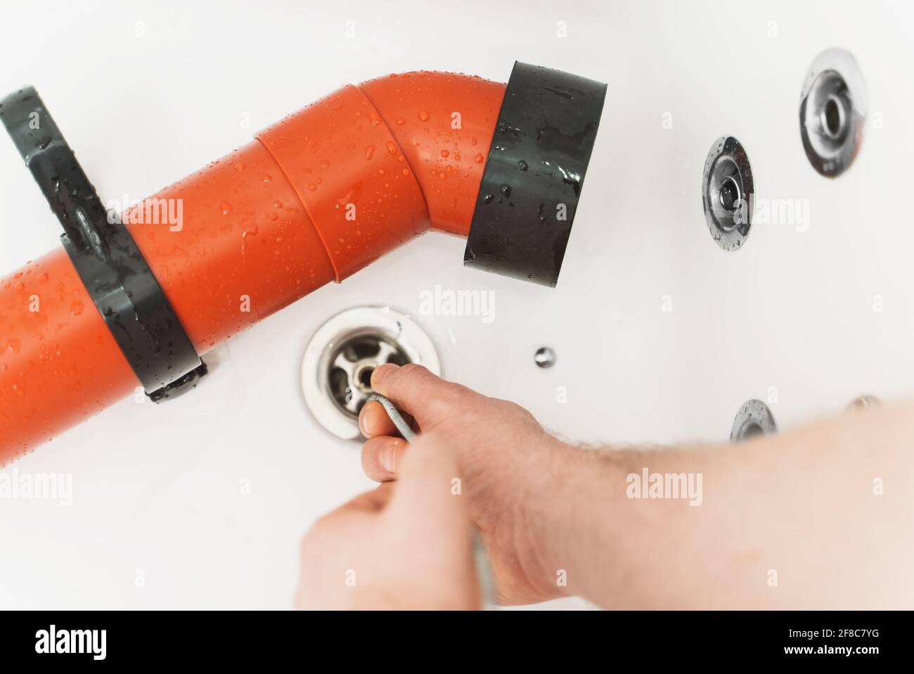 Klempner, der die Badewanne mit einer Abflussschlange entklumpt hat. Stockfoto