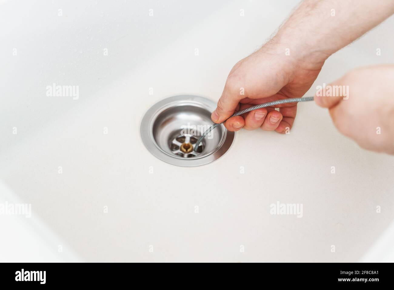 Klempner, der Abflussschlange verwendet, um das Spülbecken der Küche zu entverstopfen. Stockfoto