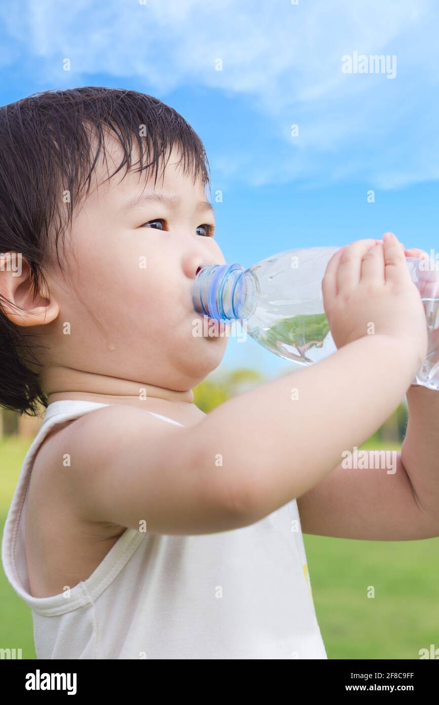 Kleines asiatisches Mädchen, das Wasser aus der Plastikflasche trinkt, nachdem es von einer Schlägerwelle im Park müde war, unter hellem Sonnenlicht und blauem Himmel im Hintergrund, im Freien Sho Stockfoto