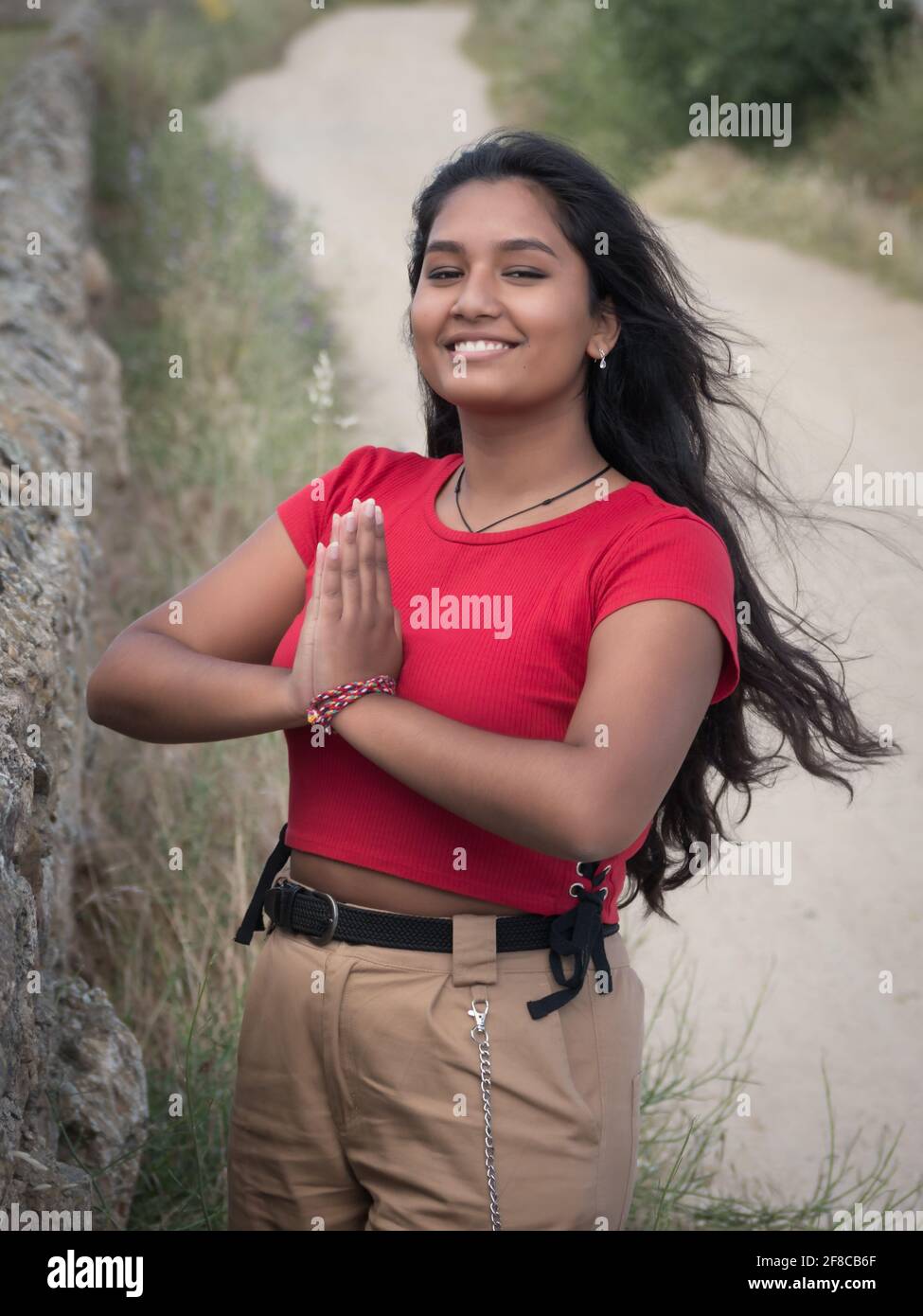 Asiatisch fröhlich aussehende Frau in Namaste Saluting Geste mit Sandweg im Hintergrund. Stockfoto