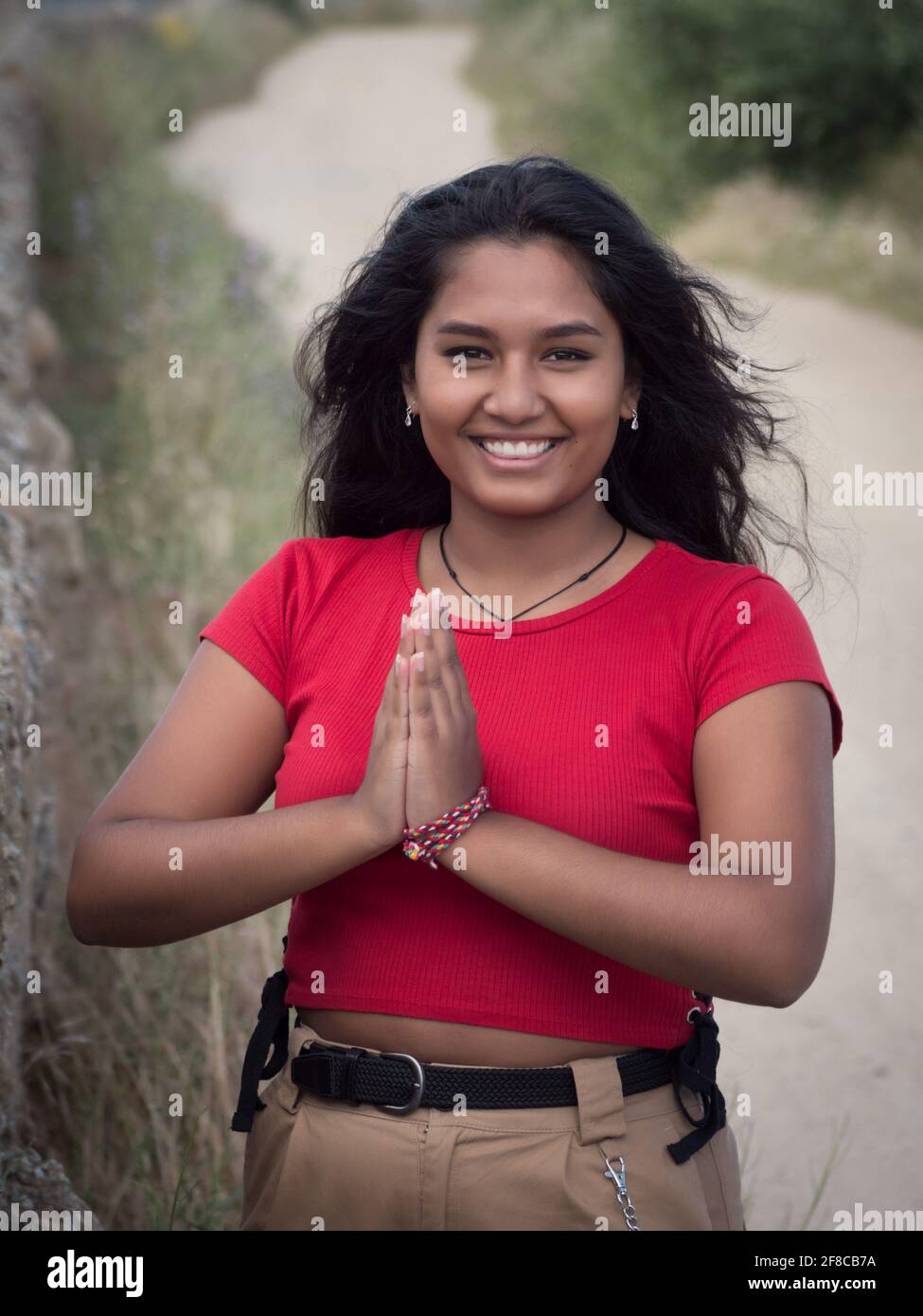 Vorderansicht der asiatisch fröhlich aussehenden Frau in Namaste Saluting Geste mit Sandweg im Hintergrund. Stockfoto