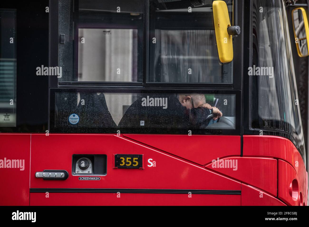 Ein Busfahrer schläft auf seinem Fahrersitz zwischen den Strecken, London, Großbritannien Stockfoto