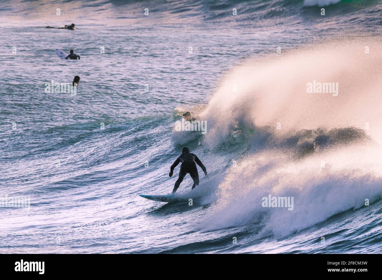 Ein Surfer, der eine große Welle als Spray reitet, wird in Fistral Bay in Newquay in Cornwall von starkem Wind vom Kamm geblasen. Stockfoto