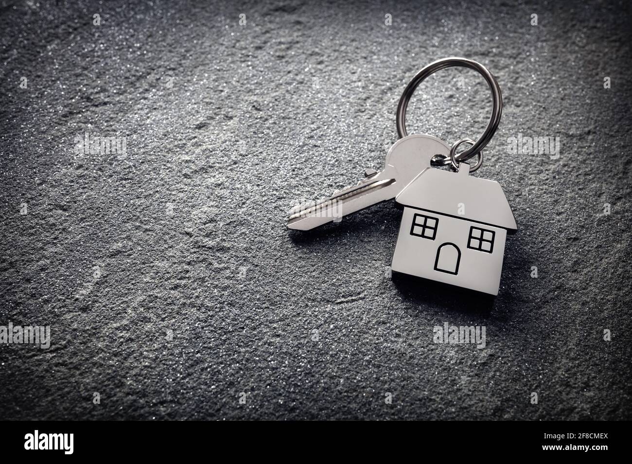 Hausschlüssel auf einem hausförmigen Schlüsselanhänger auf Stein Konzept für Immobilien, Umzug nach Hause oder Vermietung von Immobilien Stockfoto