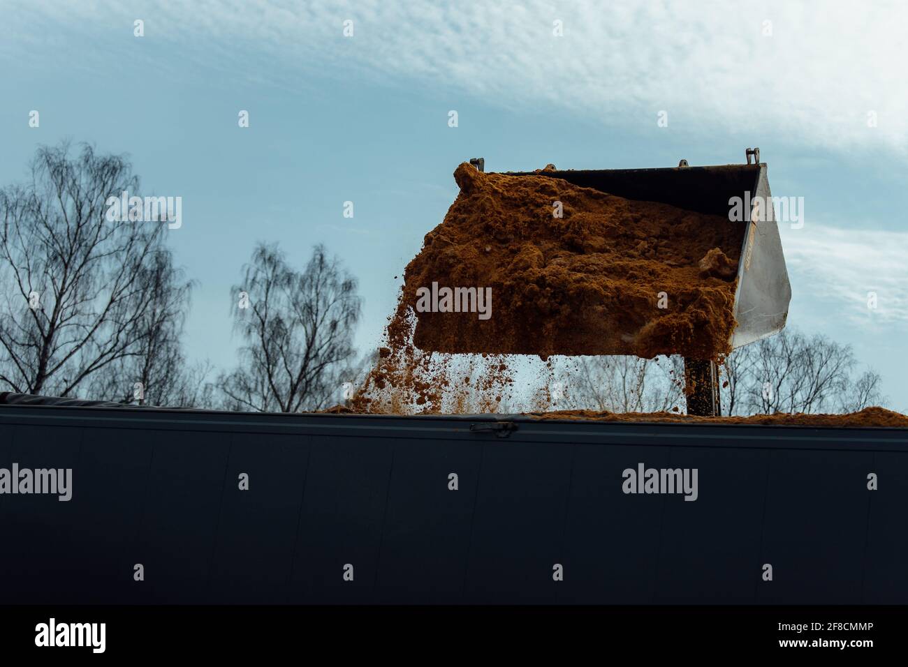 Ein Industriebagger belädt den LKW-Körper mit Rohstoffen. Gieße Sand aus dem Eimer. Transport liefert Ladung in der Fabrik Stockfoto