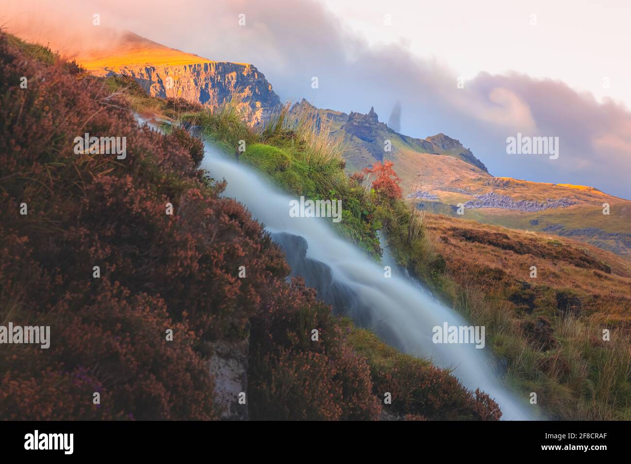 Goldenes Licht und lebhafter, farbenfroher Sonnenuntergang- oder Sonnenaufgangshimmel über der dramatischen Landschaft des Old man of Storr mit dem Wasserfall Bride's Veil Falls auf der Isle of Stockfoto