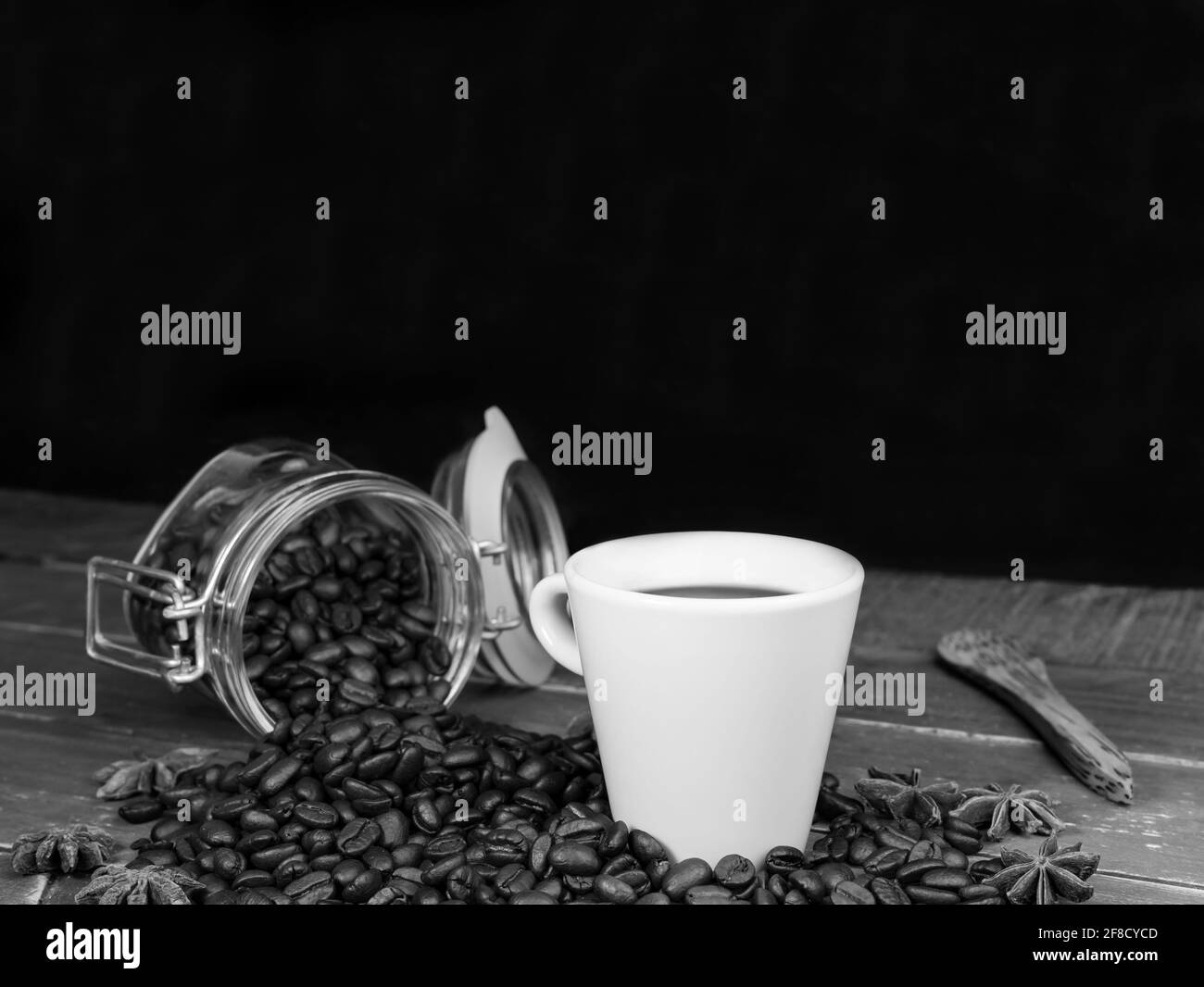 Weiße Tasse Kaffee und Kaffeebohnen auf Holztisch. Schwarz-weiße Fotografie, Konzept von rustikalem Kaffee auf dunklem Hintergrund mit Kopierraum. Stockfoto