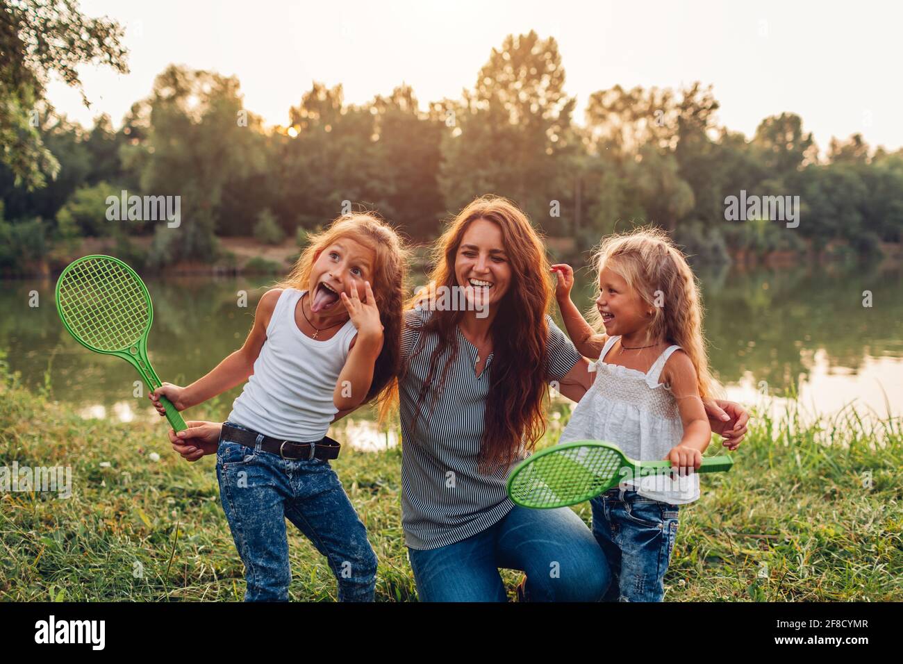 Muttertag. Die Familie hat Spaß, nachdem sie Badminton am Summer River gespielt hat. Mutter lachte und grimazing mit Töchtern im Freien. Stockfoto