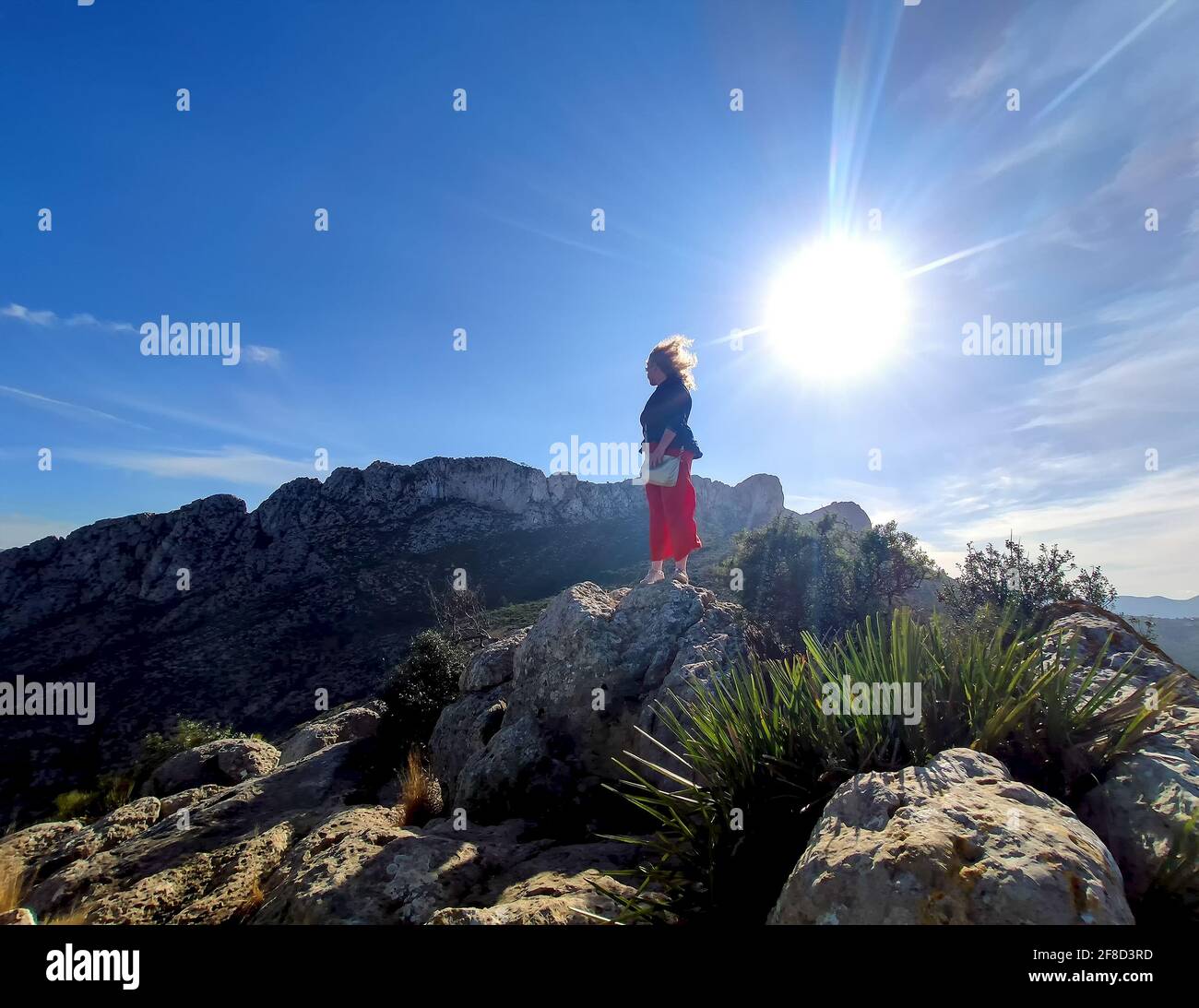 Reife Rothaarige Frau mit Hintergrundbeleuchtung und windgeblasenem Haar auf dem Berg CIM Penya Roja, Els Poblets, Valenciana, Alicante, Spanien Stockfoto