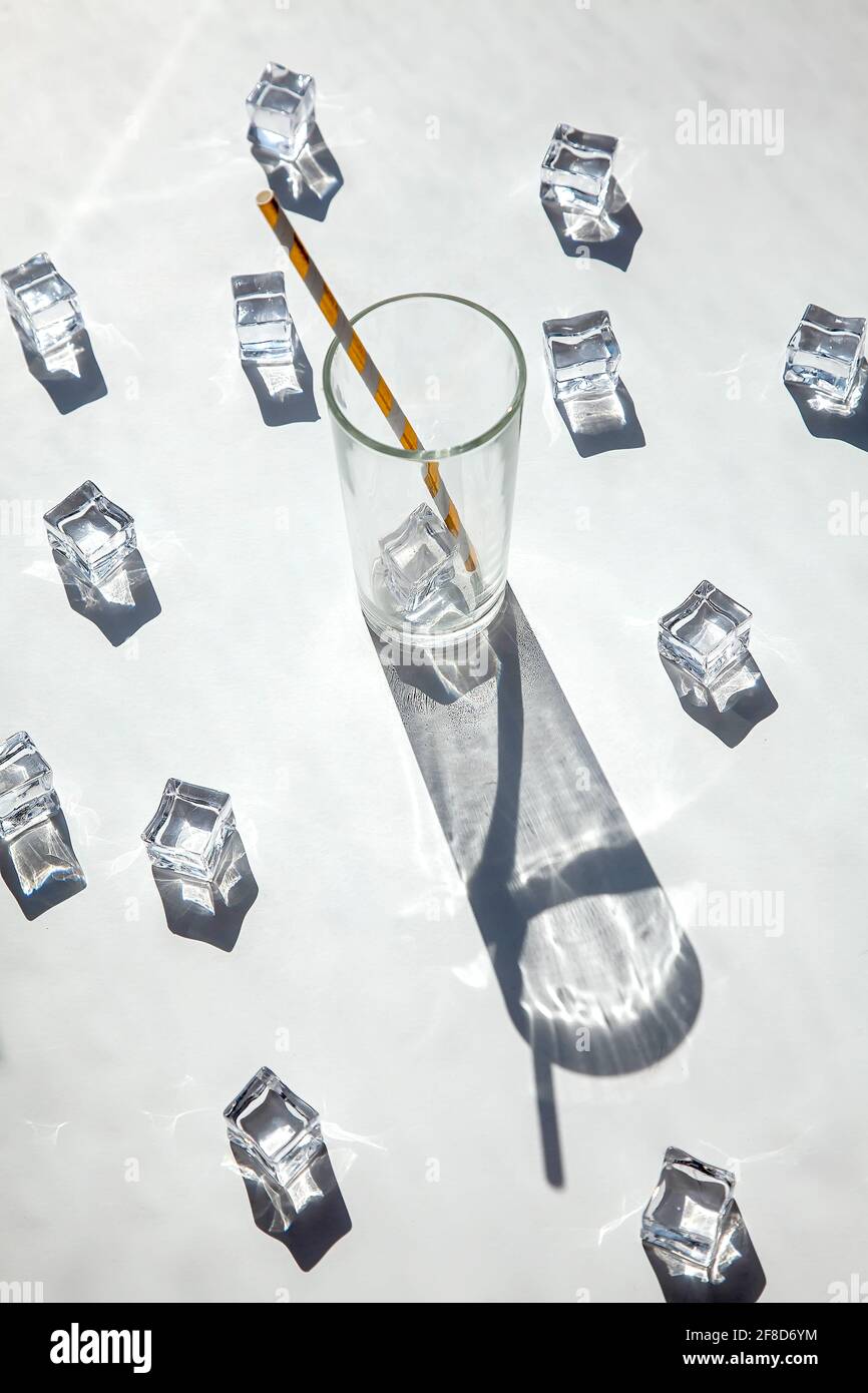 Ein leeres Glas mit Eiswürfeln und Sonnenschatten auf weißem Hintergrund. Solarfotografie. Blick von oben, heißer Sommer und Getränkekonzept. Stockfoto