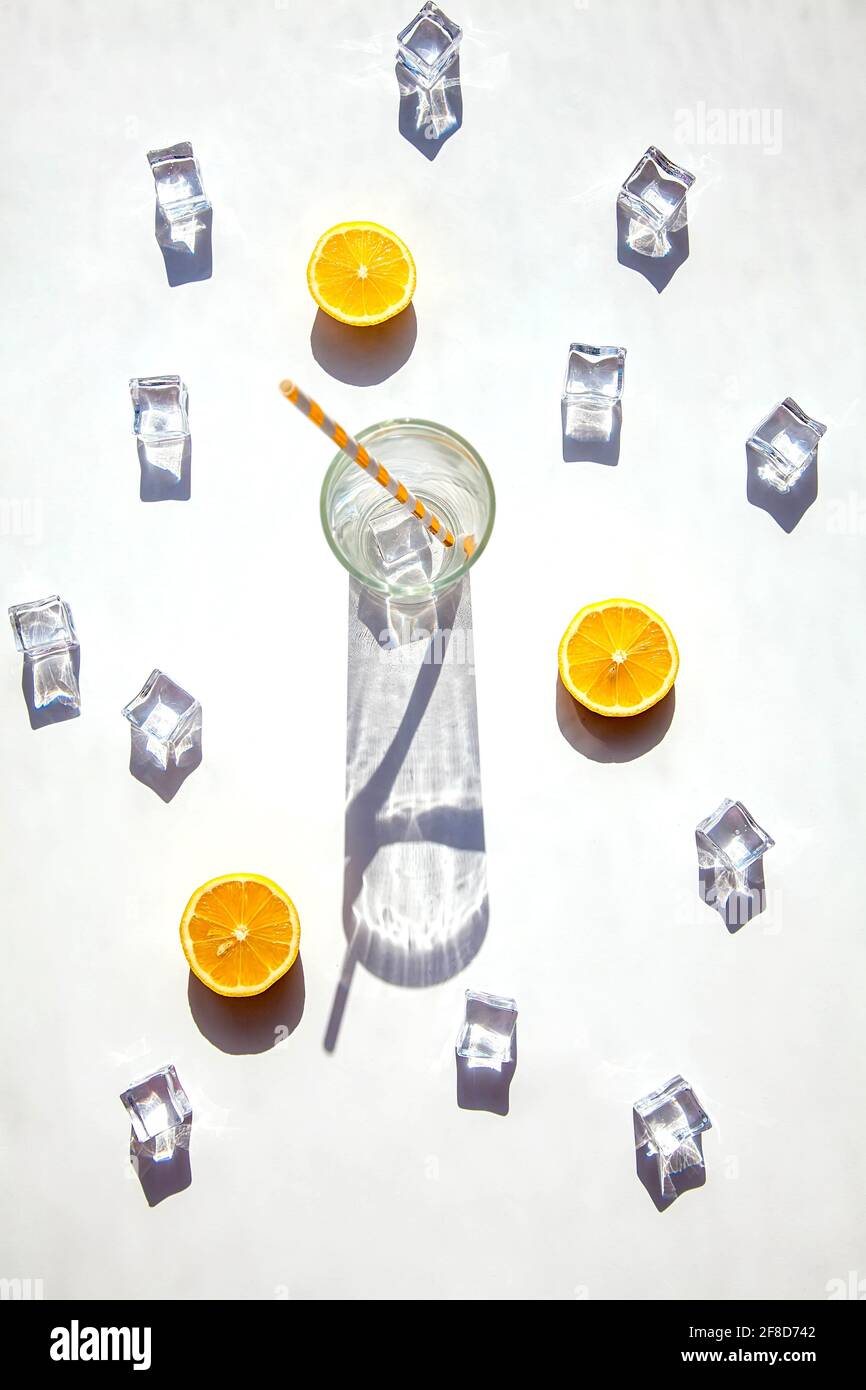 Ein leeres Glas mit einem großen Schatten, Eiswürfeln und orangefarbenen Scheiben auf weißem Hintergrund. Solarfotografie. Blick von oben, heißer Sommer und Getränk Conce Stockfoto