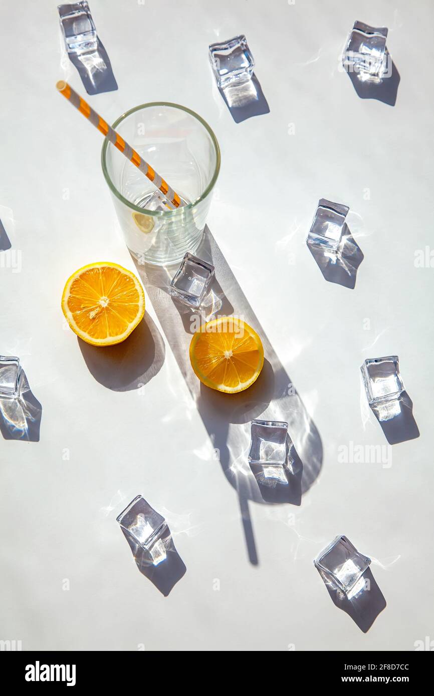 Ein leeres Glas mit einem großen Schatten, Eiswürfeln und orangefarbenen Scheiben auf weißem Hintergrund. Solarfotografie. Blick von oben, heißer Sommer und Getränk Conce Stockfoto