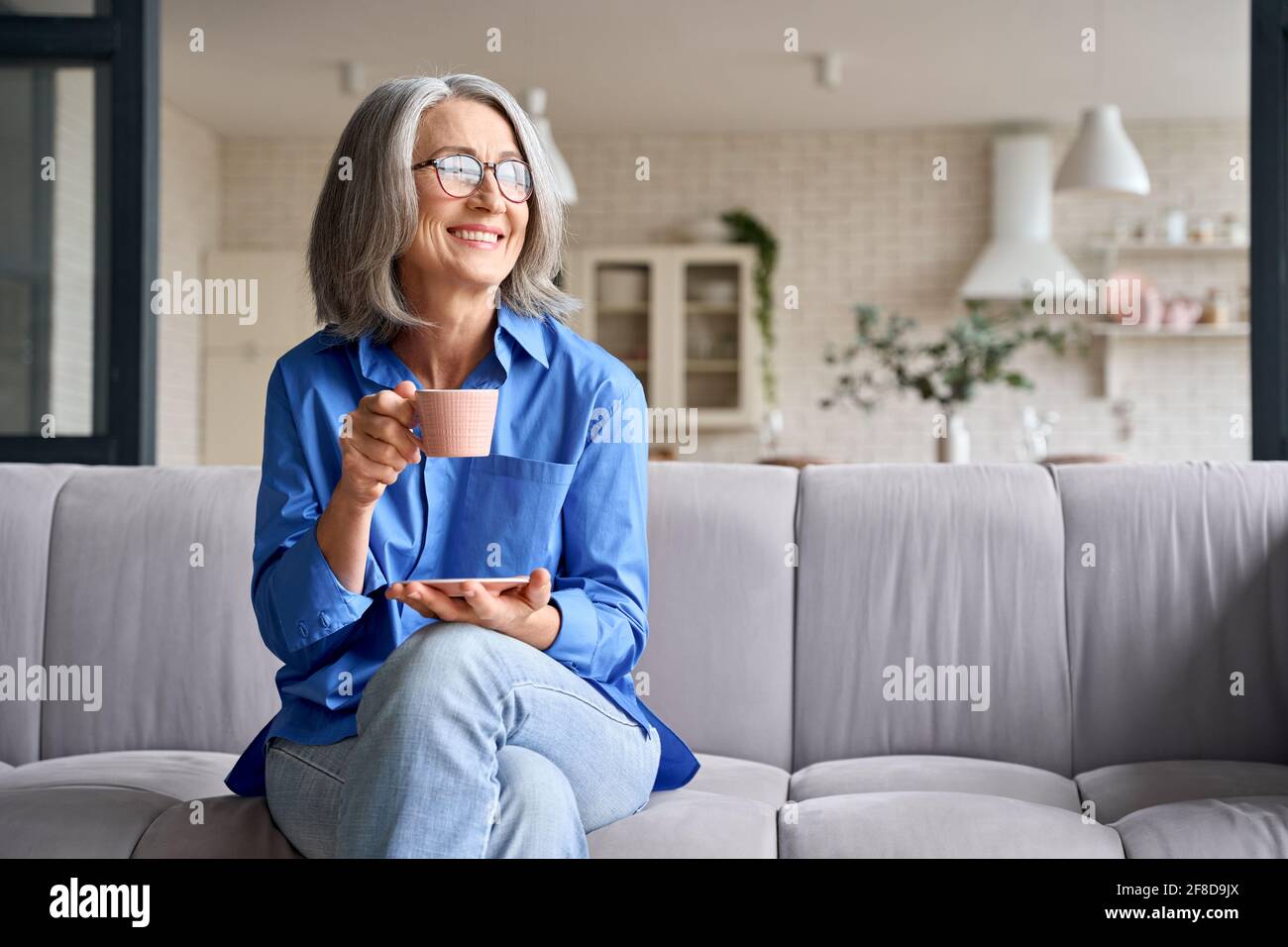Ältere lächelnde 60s Frau Porträt zu Hause Blick weg mit einer Tasse Tee, Kaffee. Stockfoto