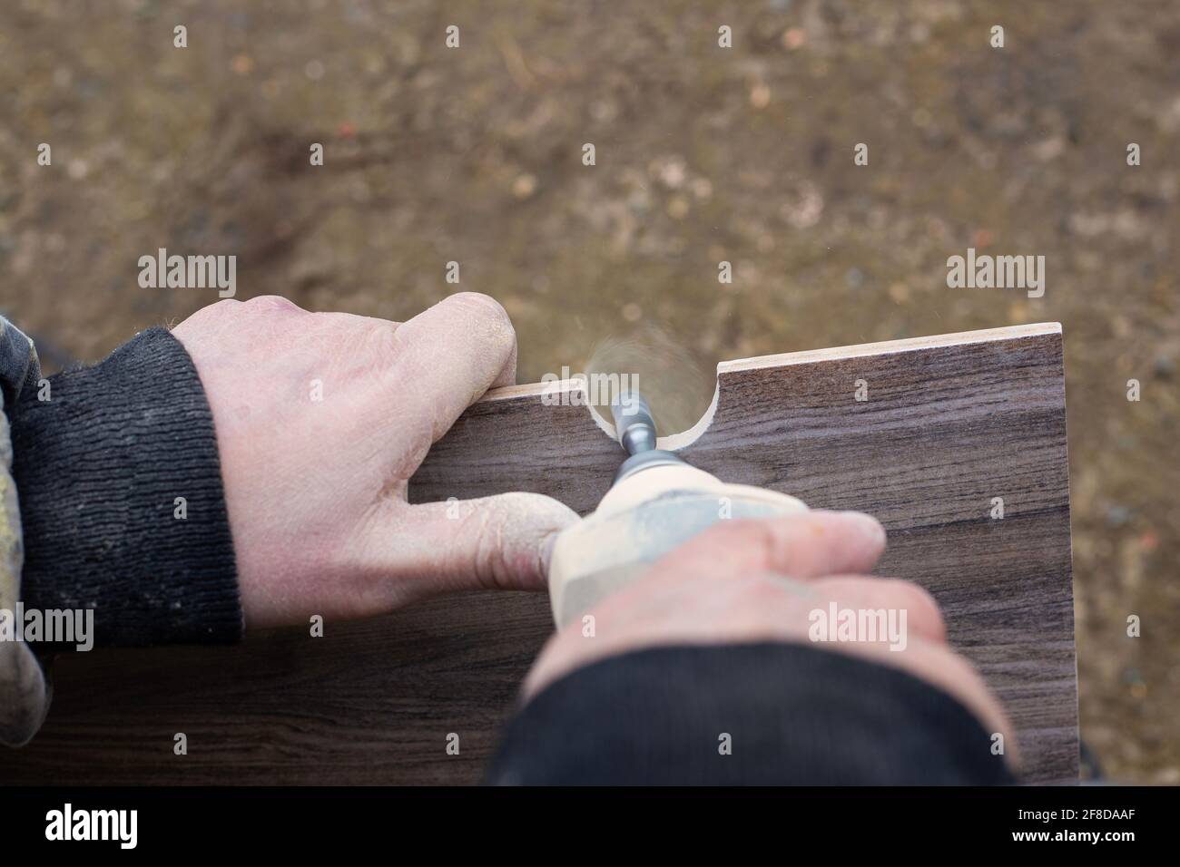 Ein Mann fräst ein Loch in einer Keramikfliese für Sanitärartikel mit einem Mini-Elektroschleifer.Renovierung und Verkleidung des Badezimmers. Stockfoto