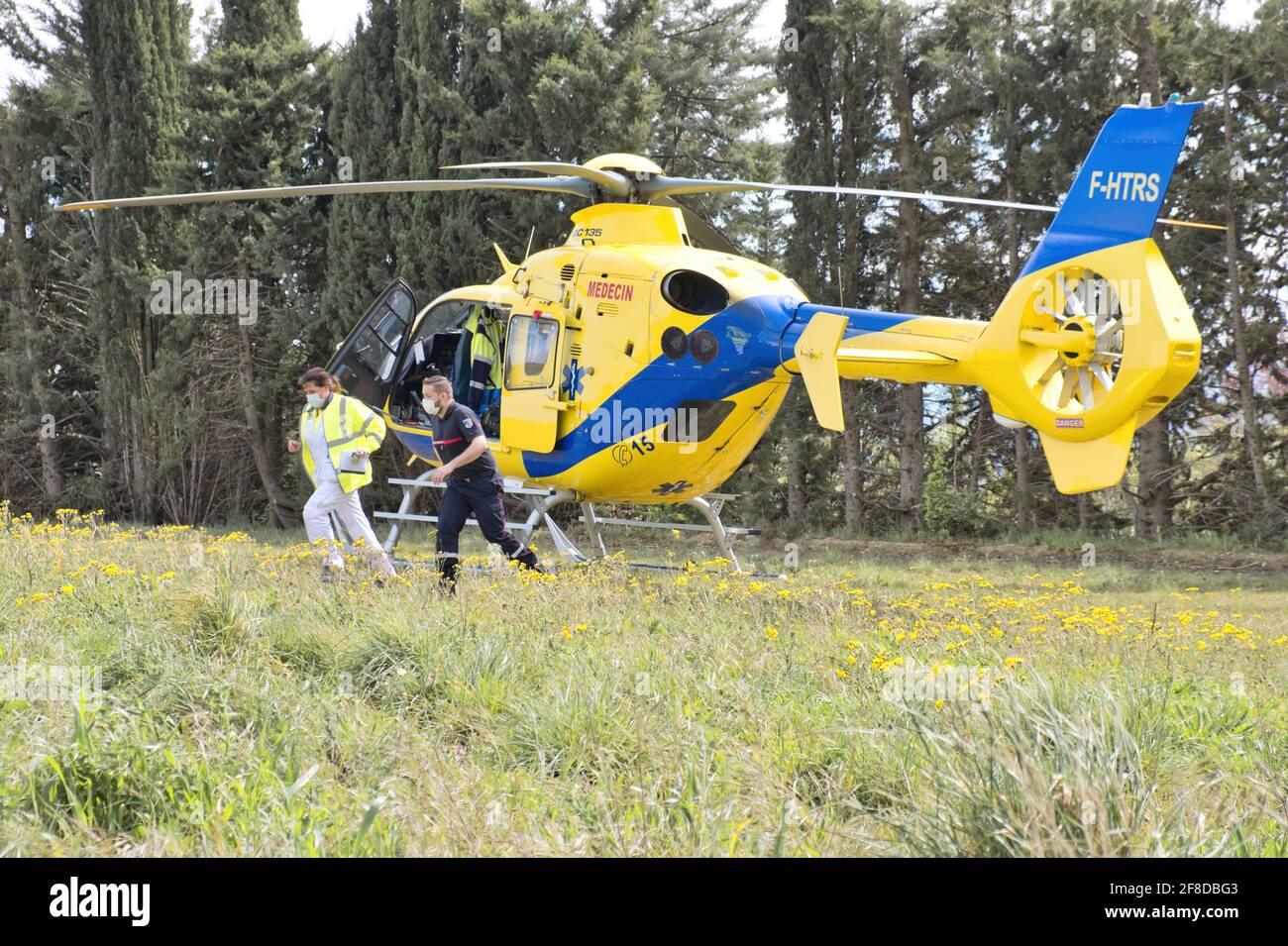 Limoux Aude France 04.13.21 zwei Sanitäter laufen von ihrem Hubschrauber aus, der auf einem Feld geparkt ist. Leuchtend gelbe Ambulanz mit blauem Streifen. Feld mit Bäumen Stockfoto