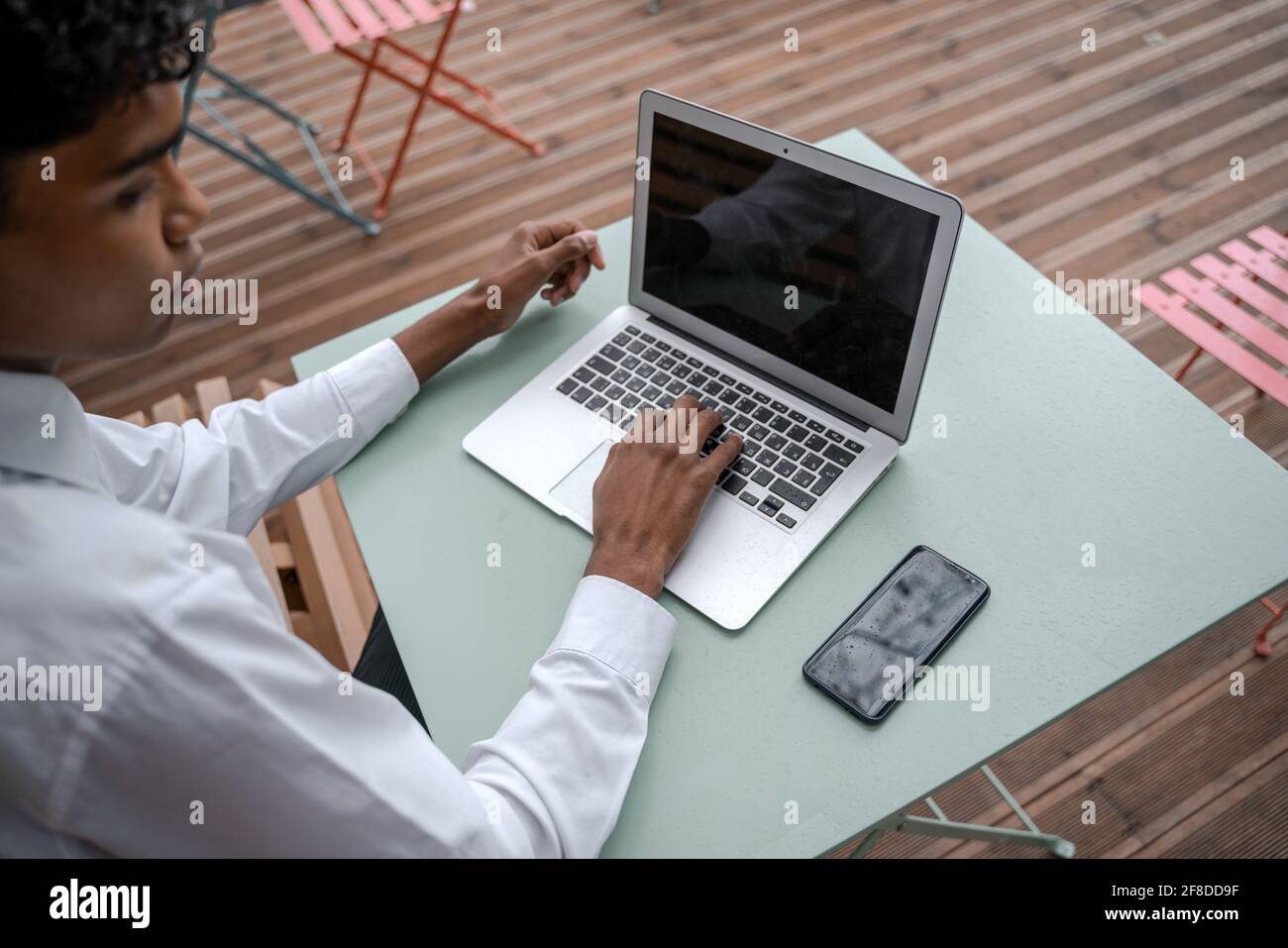Draufsicht auf den Arbeitsplatz eines schwarzen jungen Mannes. Smartphone und Laptop auf der Terrasse. Arbeiten Sie außerhalb des Büros, arbeiten Sie an einem anderen Ort oder studieren Sie das Konzept Stockfoto