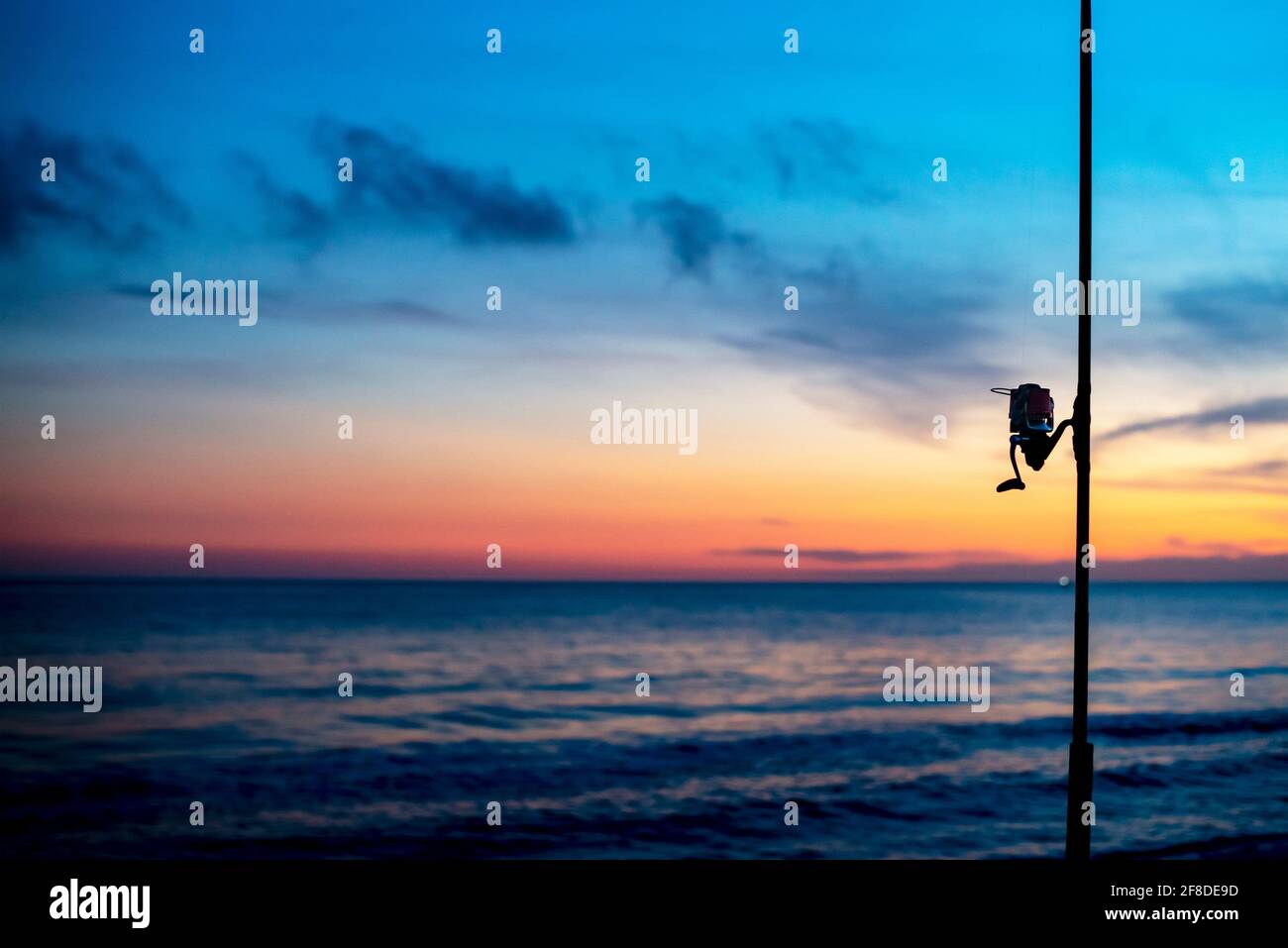 Detail der Angelrolle am Strand während des Sonnenuntergangs mit Unfokussierter Hintergrund des Meeres und farbenfroher Himmel Stockfoto