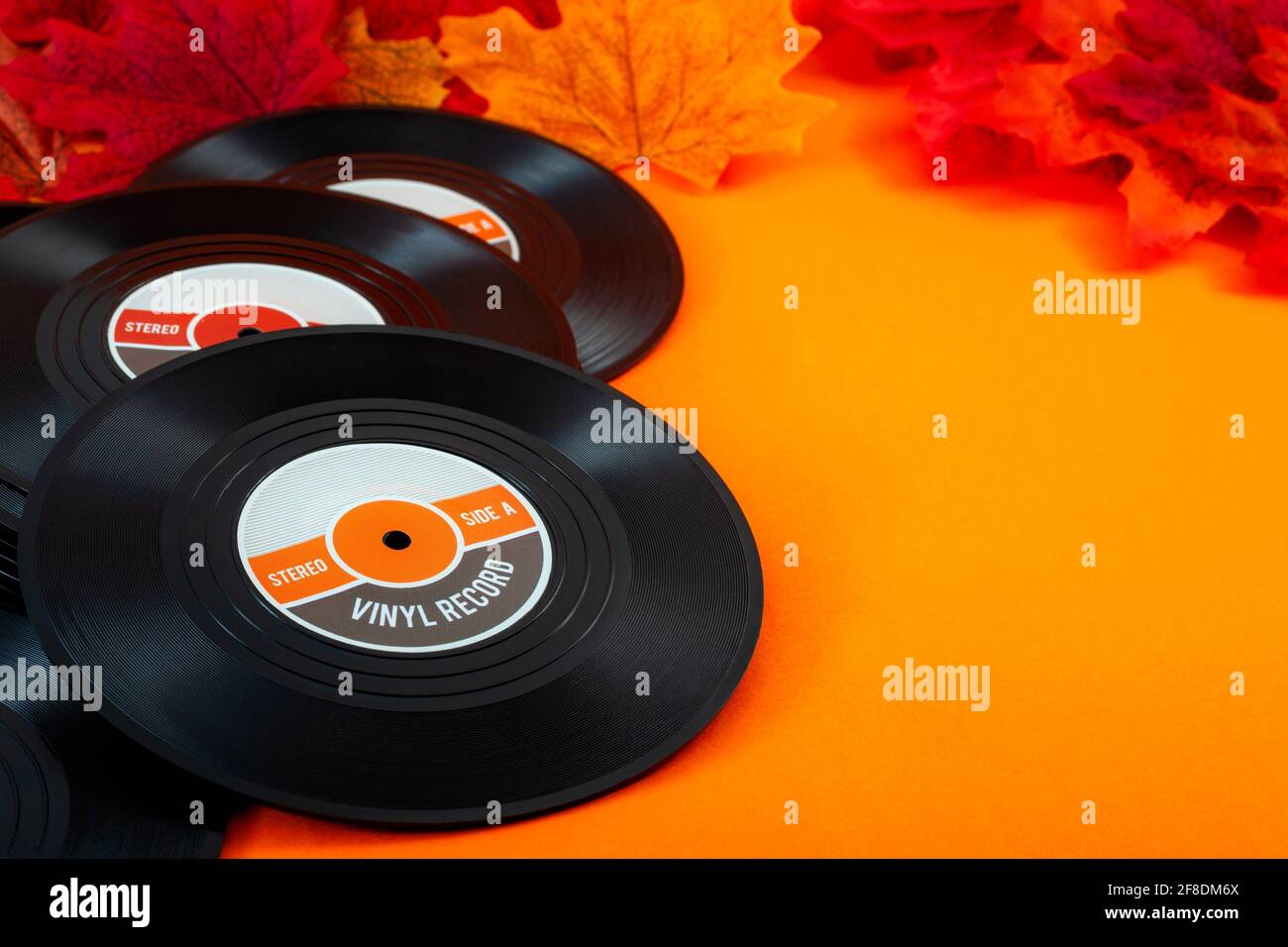 Nostalgische Songs, Herbstmusik und melandiges Konzept mit Vintage-Vinyl-Schallplatten, umgeben von herbstlichen roten und gelben Blättern auf orangefarbenem Hintergrund mit Cop Stockfoto