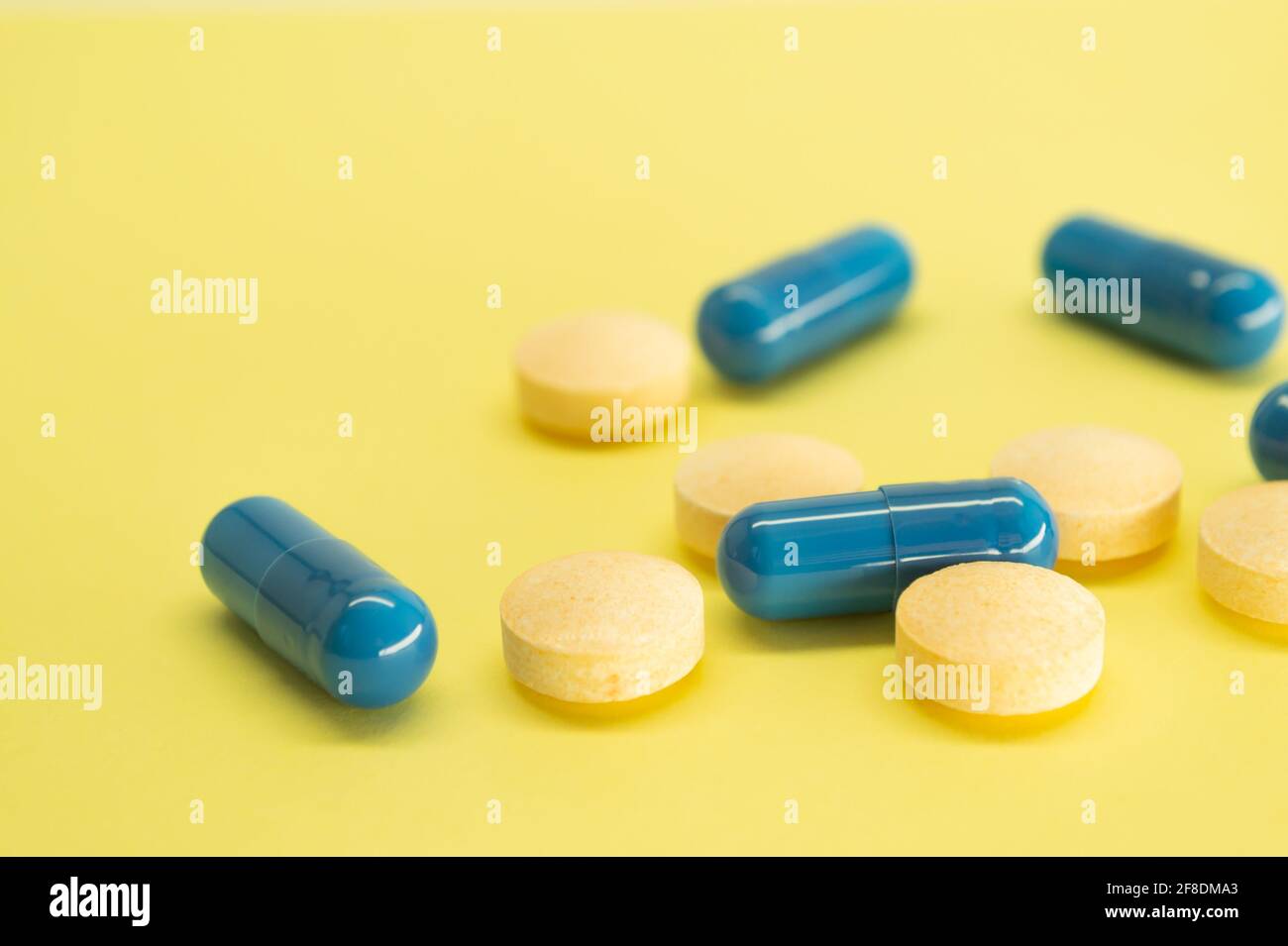 Orangefarbene Pillen und blaue Kapseln auf gelbem Hintergrund mit Platz für Text. Bild der Medizin. Gesundheitswesen. Stockfoto