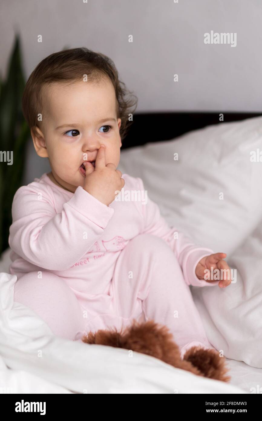 Authentische Porträt niedlich kaukasischen kleinen Säugling mollig Baby Mädchen oder Jungen in rosa schlafend beim Aufwachen Blick auf die Kamera im weißen Bett. Kinderbetreuung Stockfoto