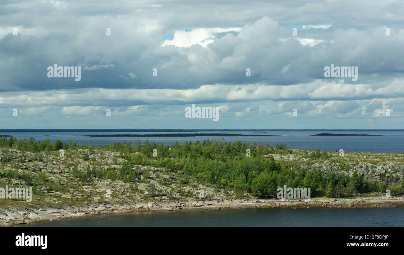 Blick auf das Meer und den Himmel von einem hohen Punkt. Raue nördliche Natur. Felsige Insel mit Wald überwuchert, dramatischer Himmel mit Regenwolken. Wunderschöne Aussicht auf Stockfoto