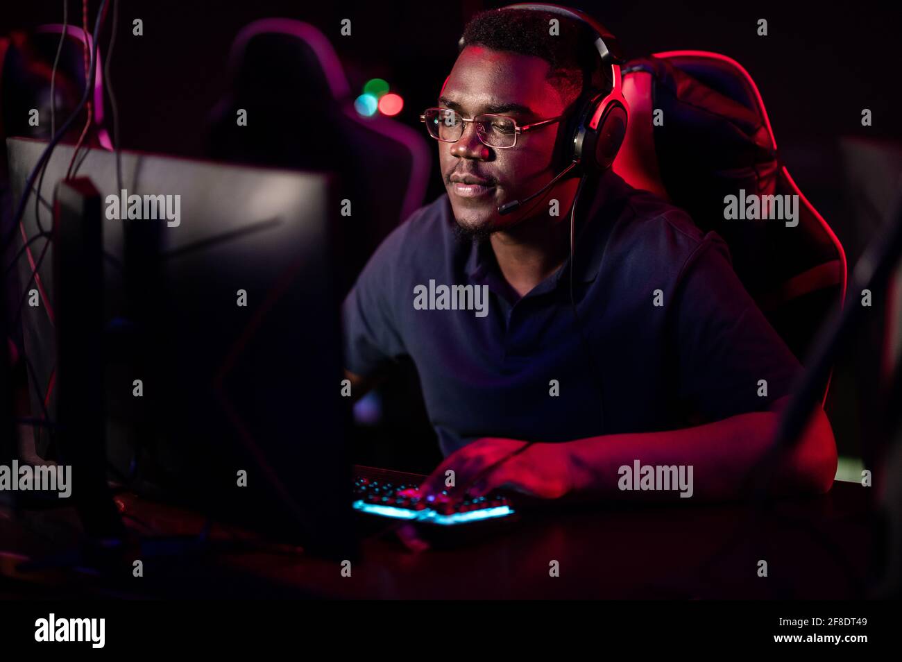 Ein afrikanischer Mann mit Kopfhörern und Brille führt während der Computerspiele-Meisterschaft einen Online-Stream. Stockfoto