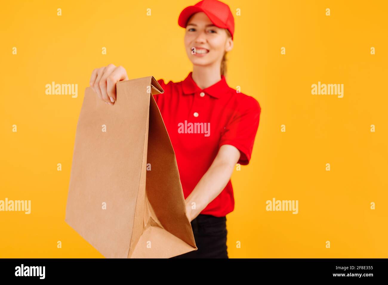 Liefererin in roter Uniform hält Papiertüte mit Essen, Mitarbeiterin in rotem T-Shirt und Mütze arbeitet als Kurier, Servicekonzept Stockfoto