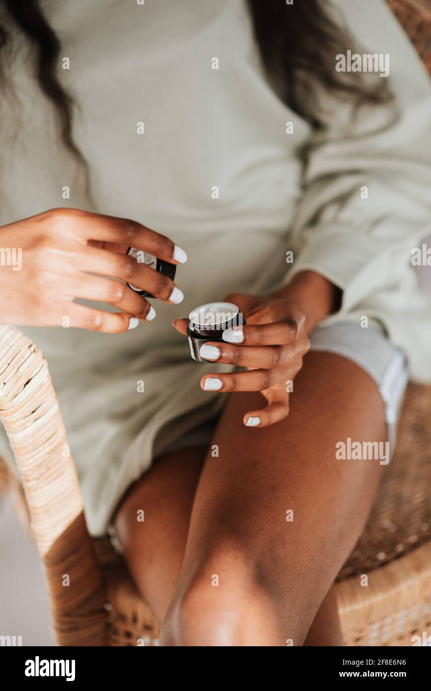 Junge afrikanische Frau hält ein Glas Lippenbalsam in der Hand Auf einem Stuhl sitzend Stockfoto