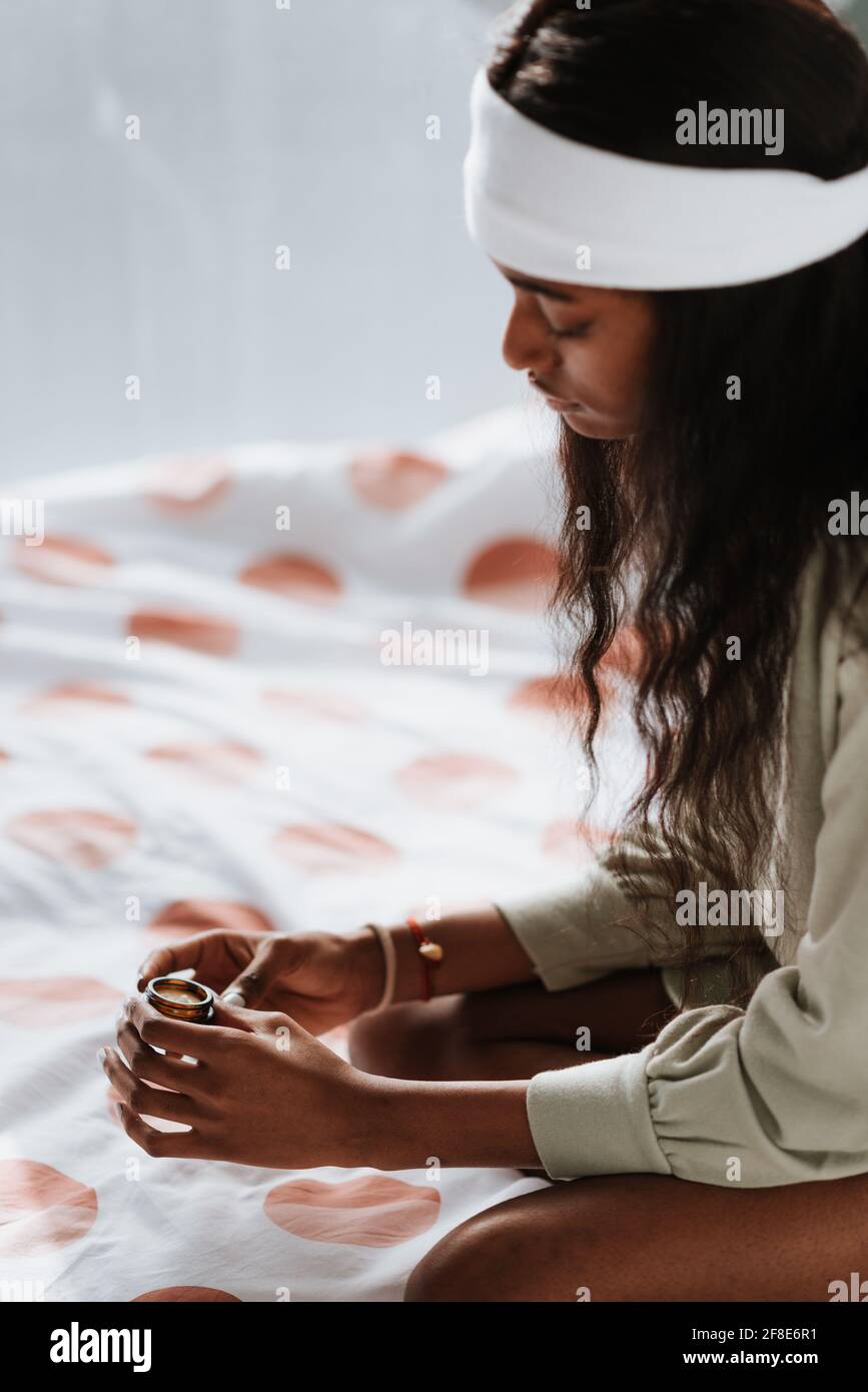 Junge afrikanische Frau hält ein Glas Lippenbalsam in der Hand Sitzen auf dem Bett Stockfoto