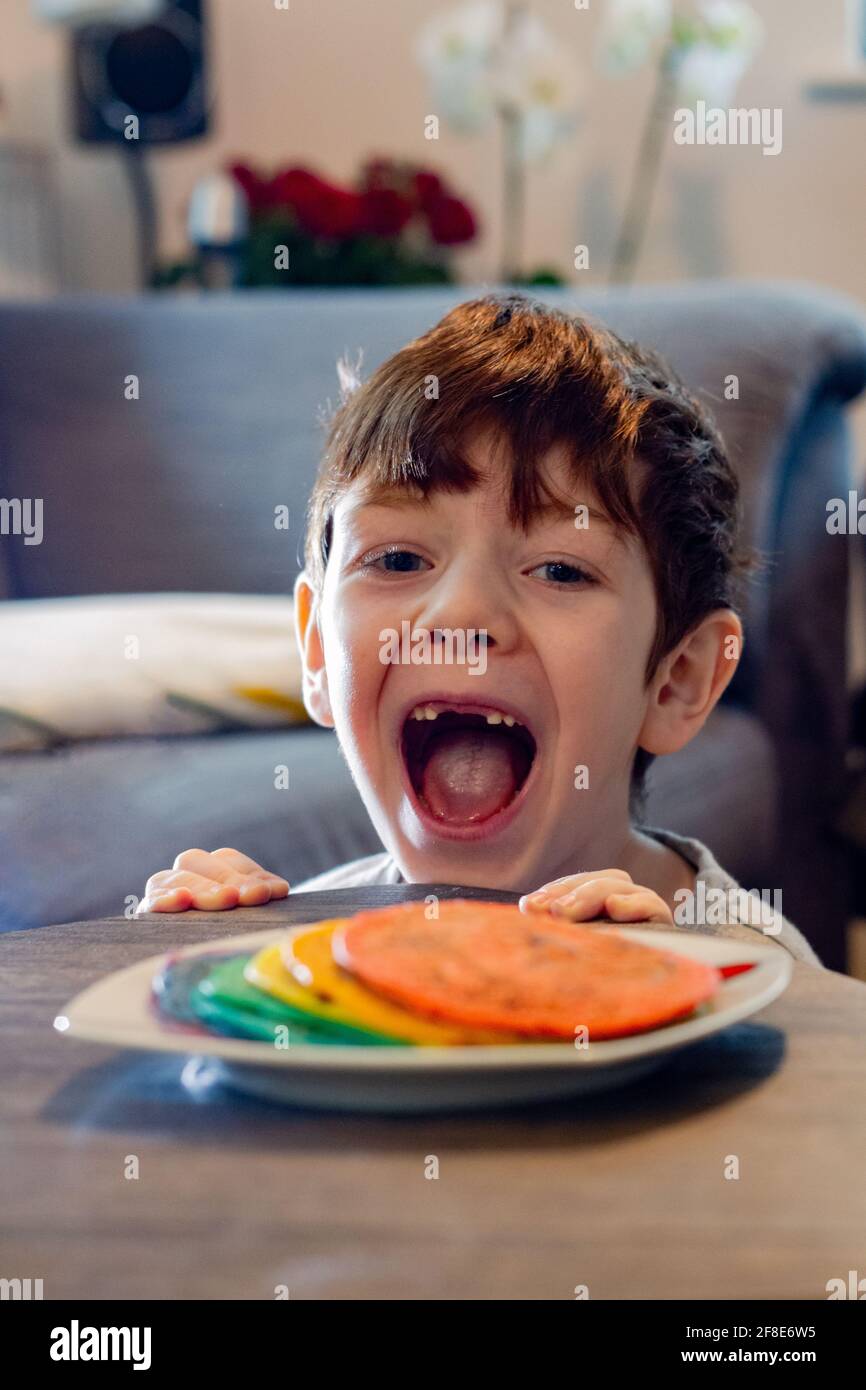 Ein süßer, blauäugiger Junge, der einen Teller mit bunten Farben ansieht Pfannkuchen mit offenem Mund Stockfoto