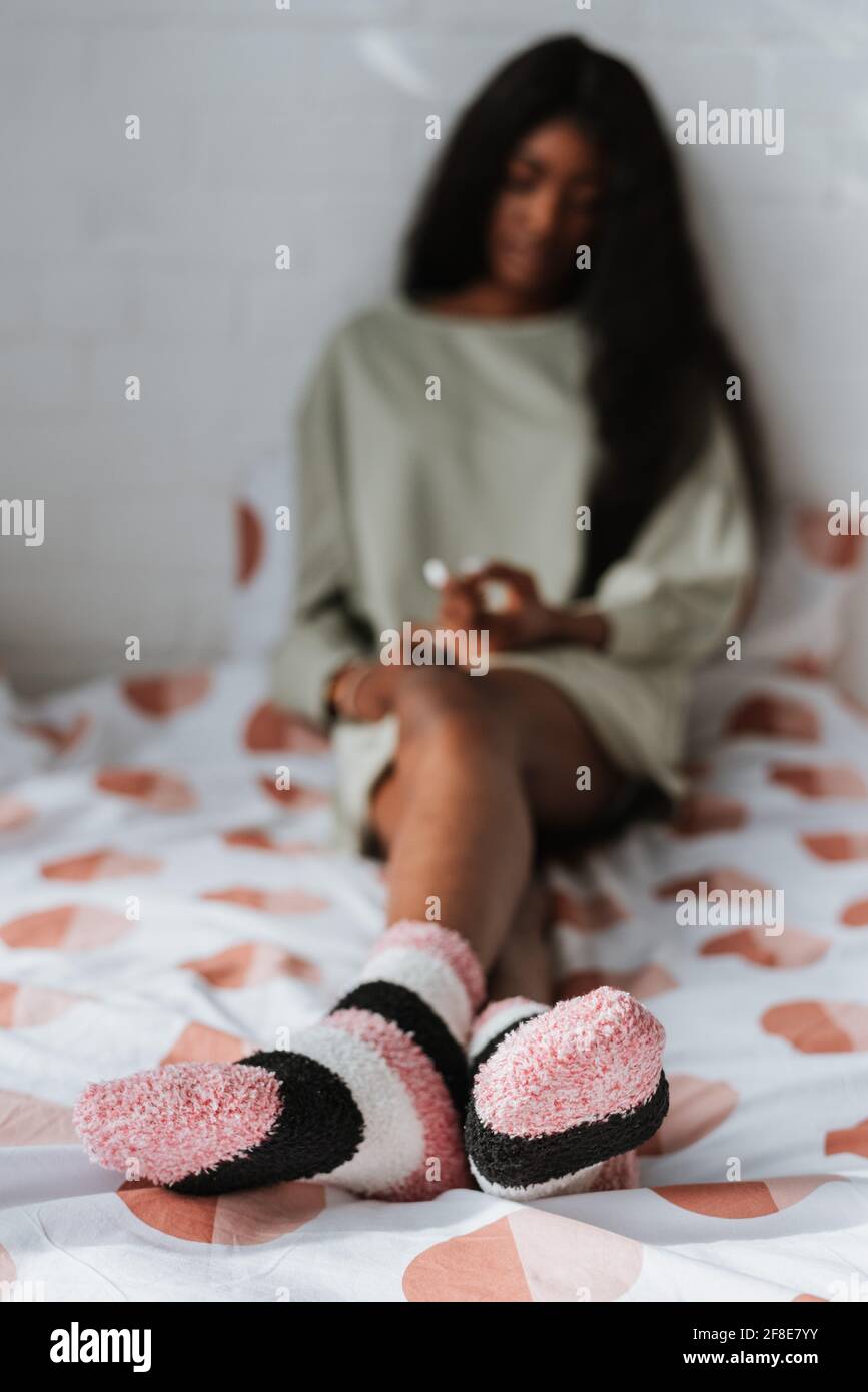 Selektive Fokusaufnahme einer jungen afrikanischen Frau, die weich trägt Gestreifte Socken sitzen auf dem Bett Stockfoto