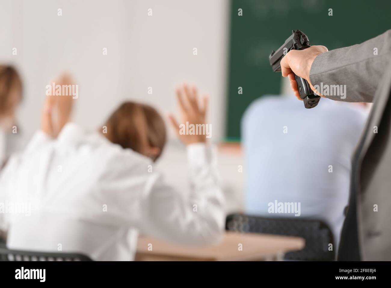 Männlicher Terrorist mit Waffe im Klassenzimmer. Problem des Schießens in der Schule Stockfoto
