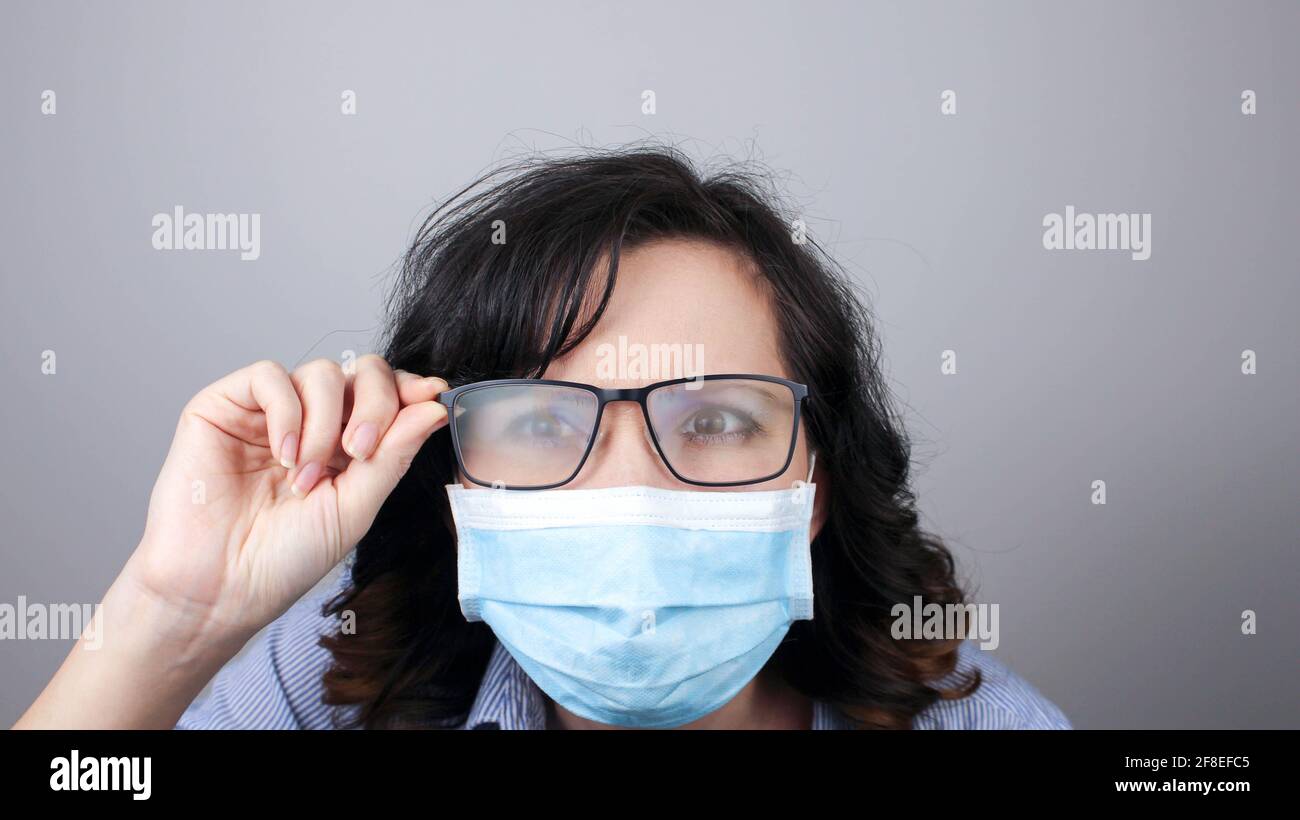 Frau trägt Schutzmaske gegen Coronavirus und vernebelte Brille. Frau in einer Maske, die in einen Spiegel schaut. Medizinische Maske, Nahaufnahme, Wählen Sie fo Stockfoto