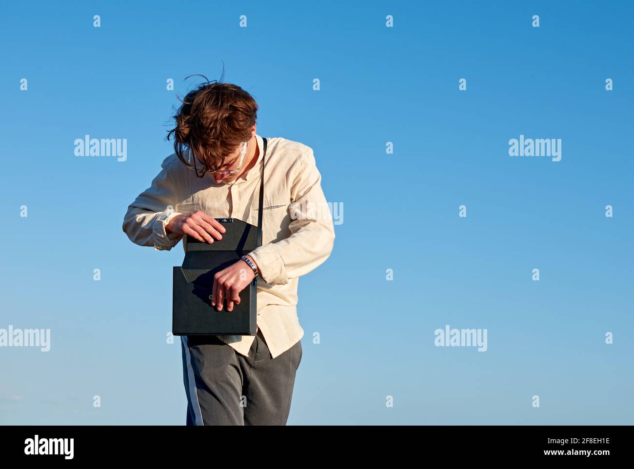 Kaukasischer Mann aus Spanien steht und öffnet seine schwarze Handtasche Auf klarem Himmel Hintergrund Stockfoto
