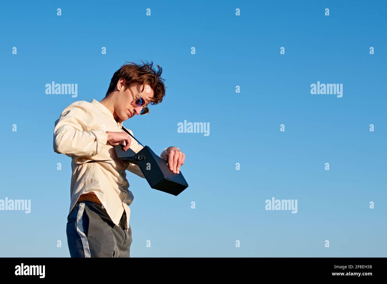 Kaukasischer Mann aus Spanien steht und setzt etwas in seine Schwarze Handtasche auf Himmel Hintergrund Stockfoto