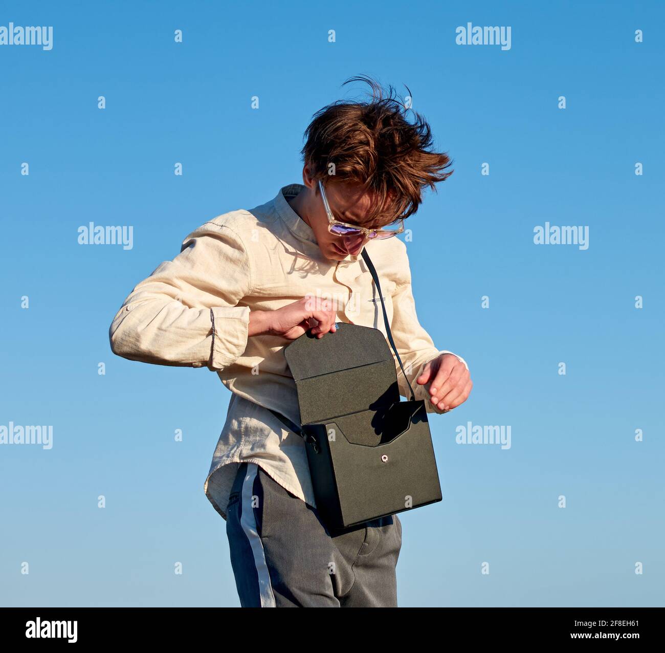 Kaukasischer Mann aus Spanien steht und schließt seine schwarze Handtasche Auf klarem Himmel Hintergrund Stockfoto