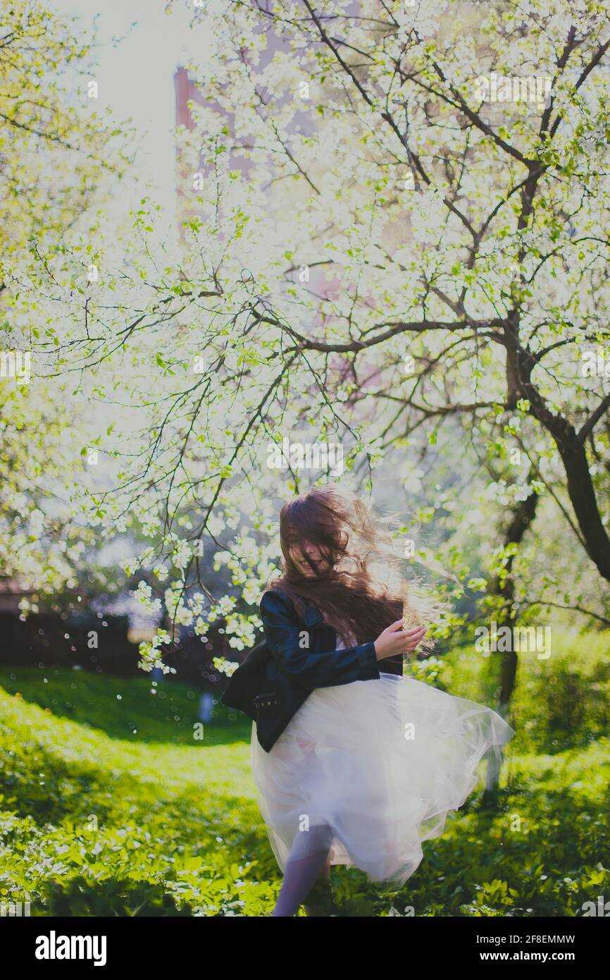 Kleines Mädchen in schwarzer Jacke und weißem Kleid tanzen in Der Kirschgarten im Frühling Stockfoto