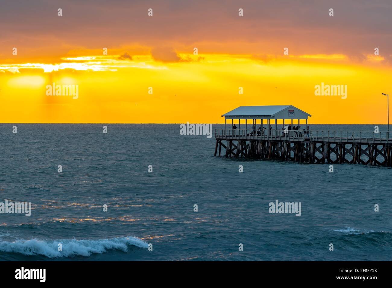 Adelaide, Australien - 11. April 2021: Menschen, die am Henley Beach Jetty spazieren, während sie den stürmischen, dramatischen Sonnenuntergang beobachten Stockfoto