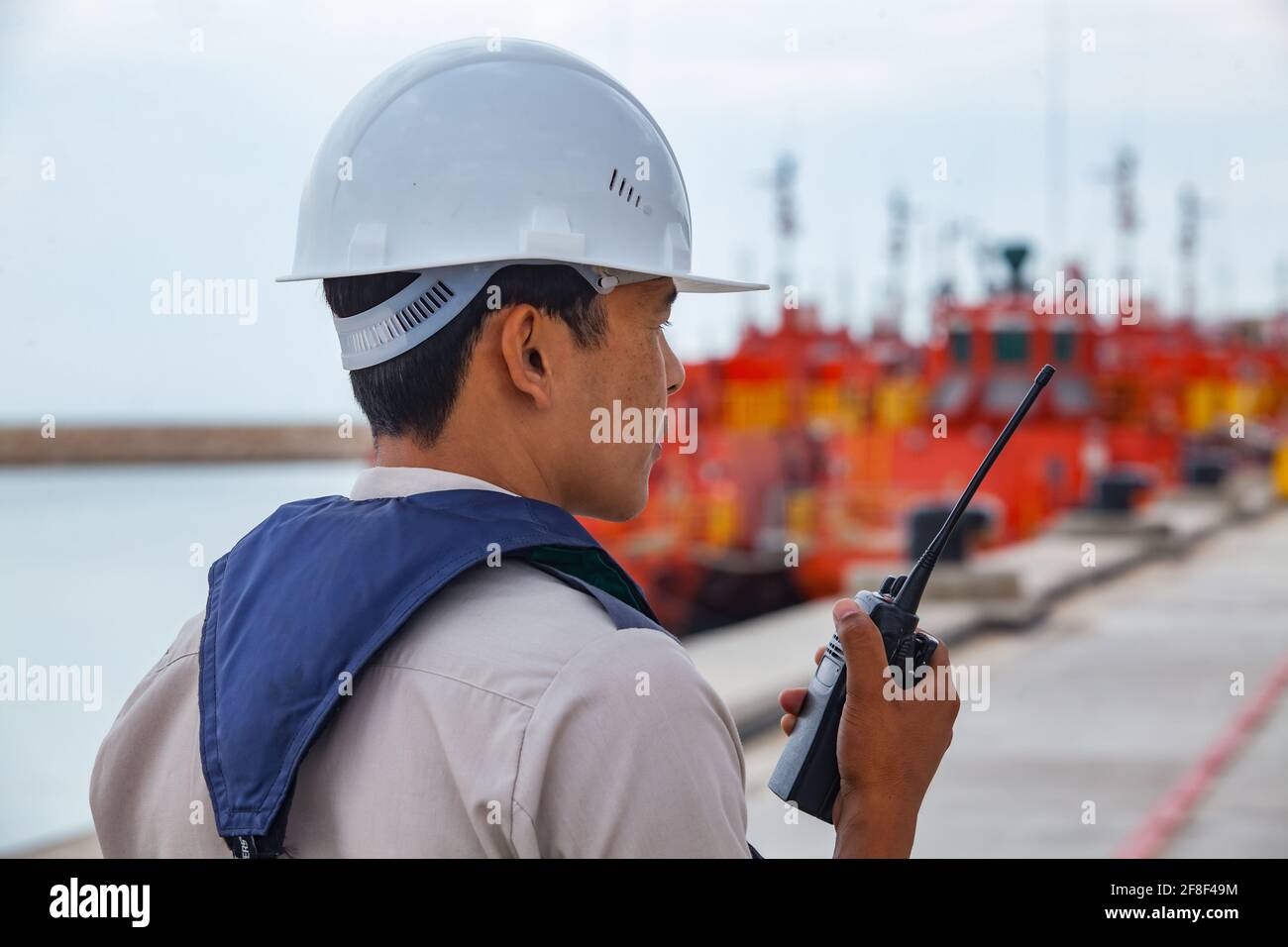 Bucht von Bautino, Mangystau, Kasachstan: Ladeterminal auf dem Kaspischen Meer. Ingenieur in Hardhut und Rettungsweste mit Radio-Set. Orange Öltankschiffe. Stockfoto