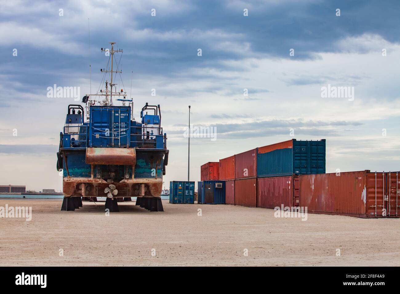 Mangystau, Kasachstan-Mai 19,2012:Bucht von Bautino, Kaspisches Meer.Schiffsreparaturwerft.Schifffahrtscontainer rechts, Schiff links.Blauer Himmel mit Wolken. Stockfoto
