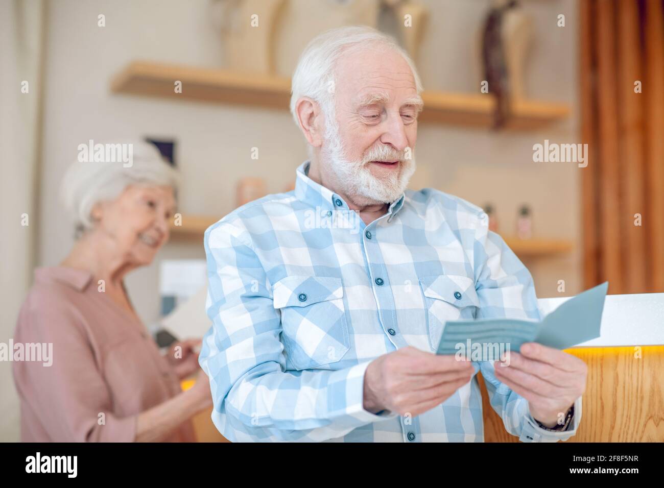 Grauhaariger bärtiger Mann, der etwas liest und dabei aussieht Stockfoto