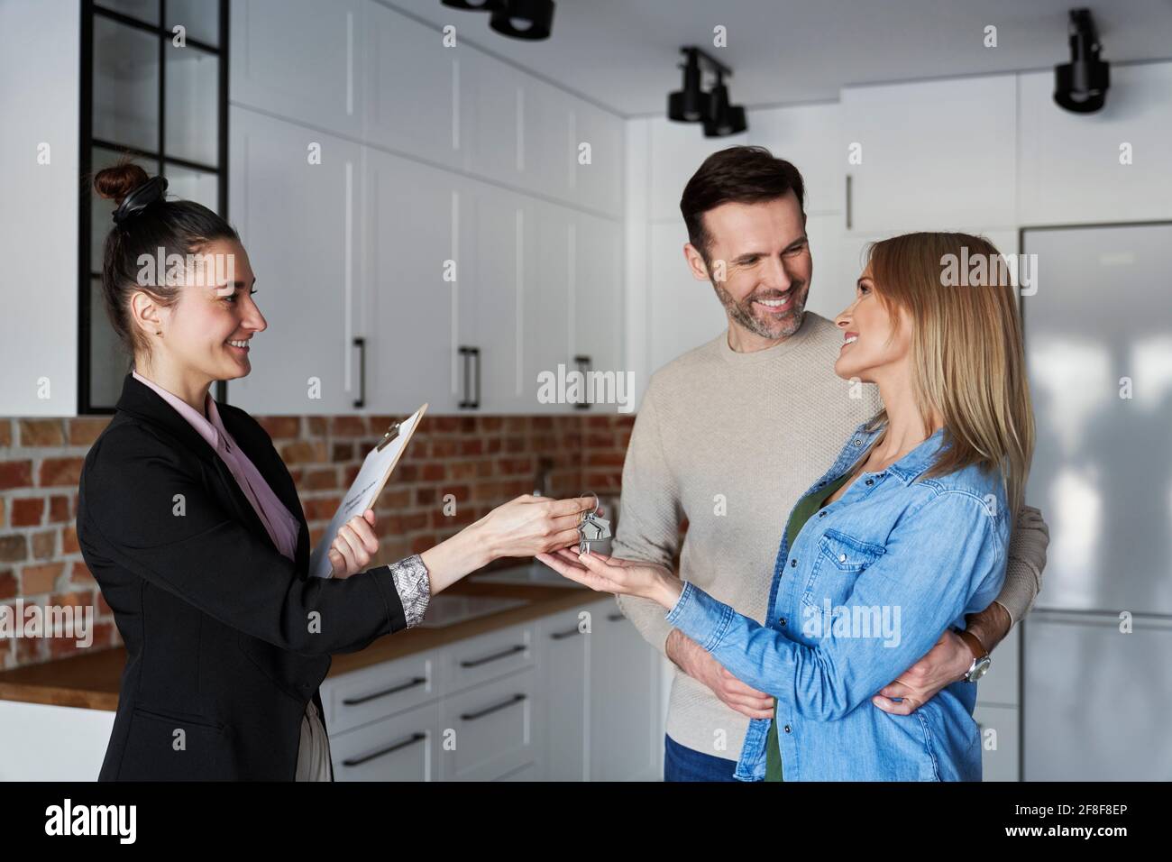 Lächelnde immobilienmakler, die dem Paar Hausschlüssel geben Stockfoto