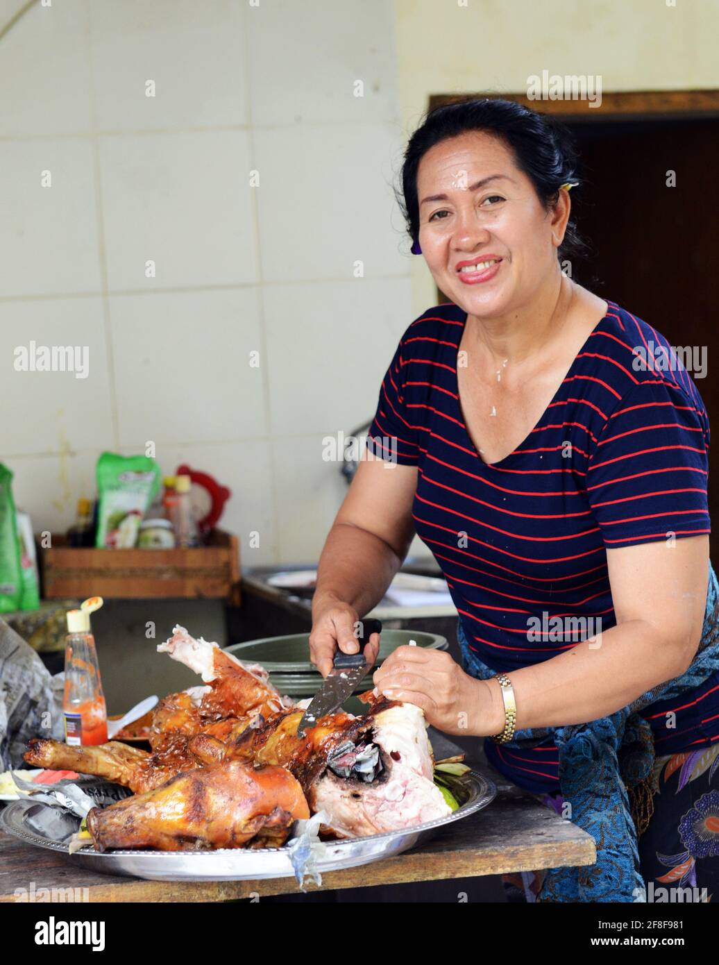 Eine balinesische Frau schneidet ein gebratenes ganzes Schweinefleisch, das während eines religiösen Festivals gekocht wurde. Stockfoto