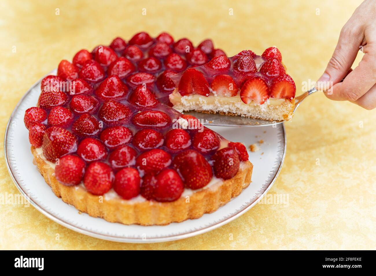 Köstlicher Erdbeerkuchen, fotografiert im Freien, auf einer gelben Tischdecke, von der ein Stück entfernt wird. Stockfoto